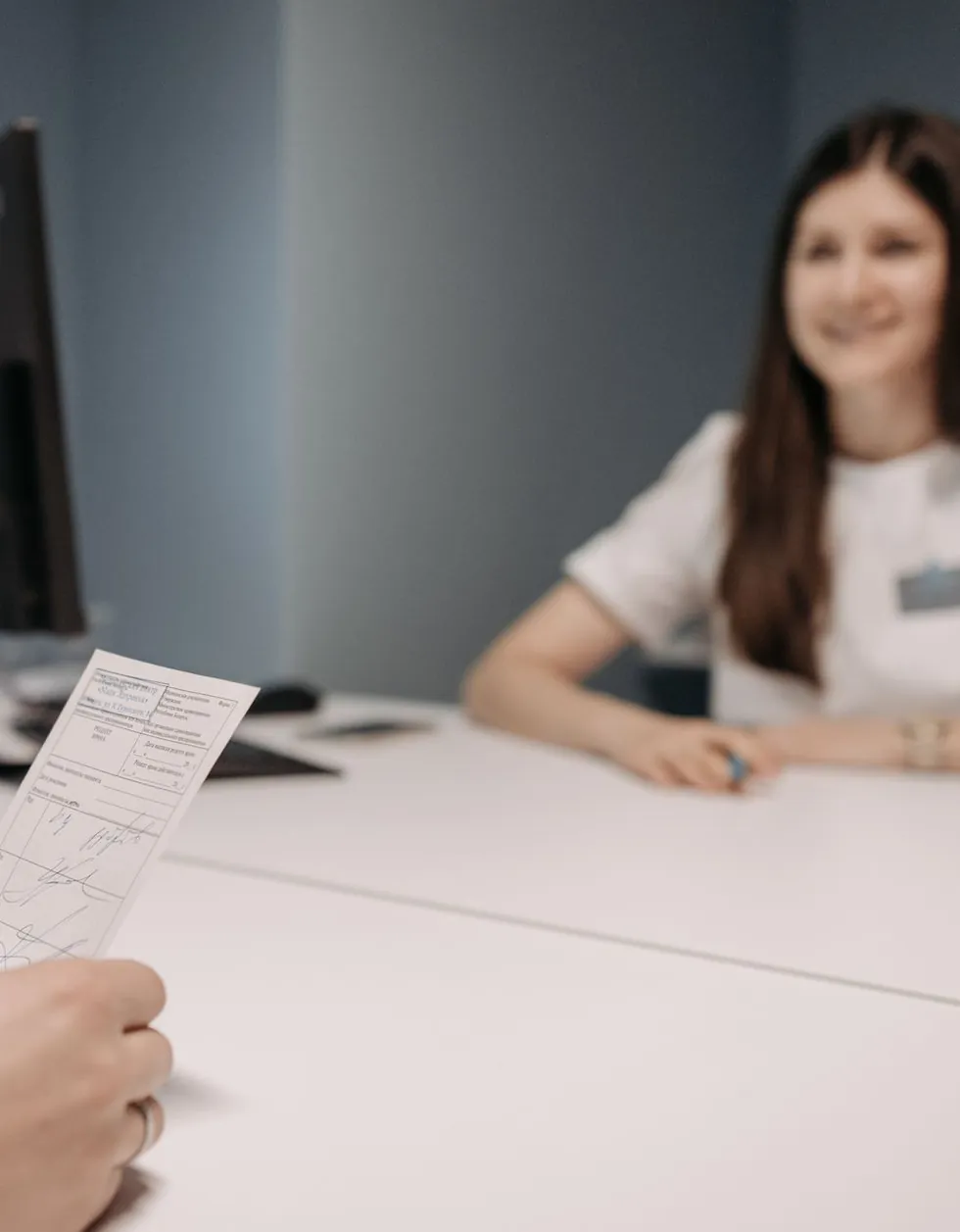 Pessoa segura a receita de papel no balcão enquanto a atendente de uniforme branco espera do outro lado